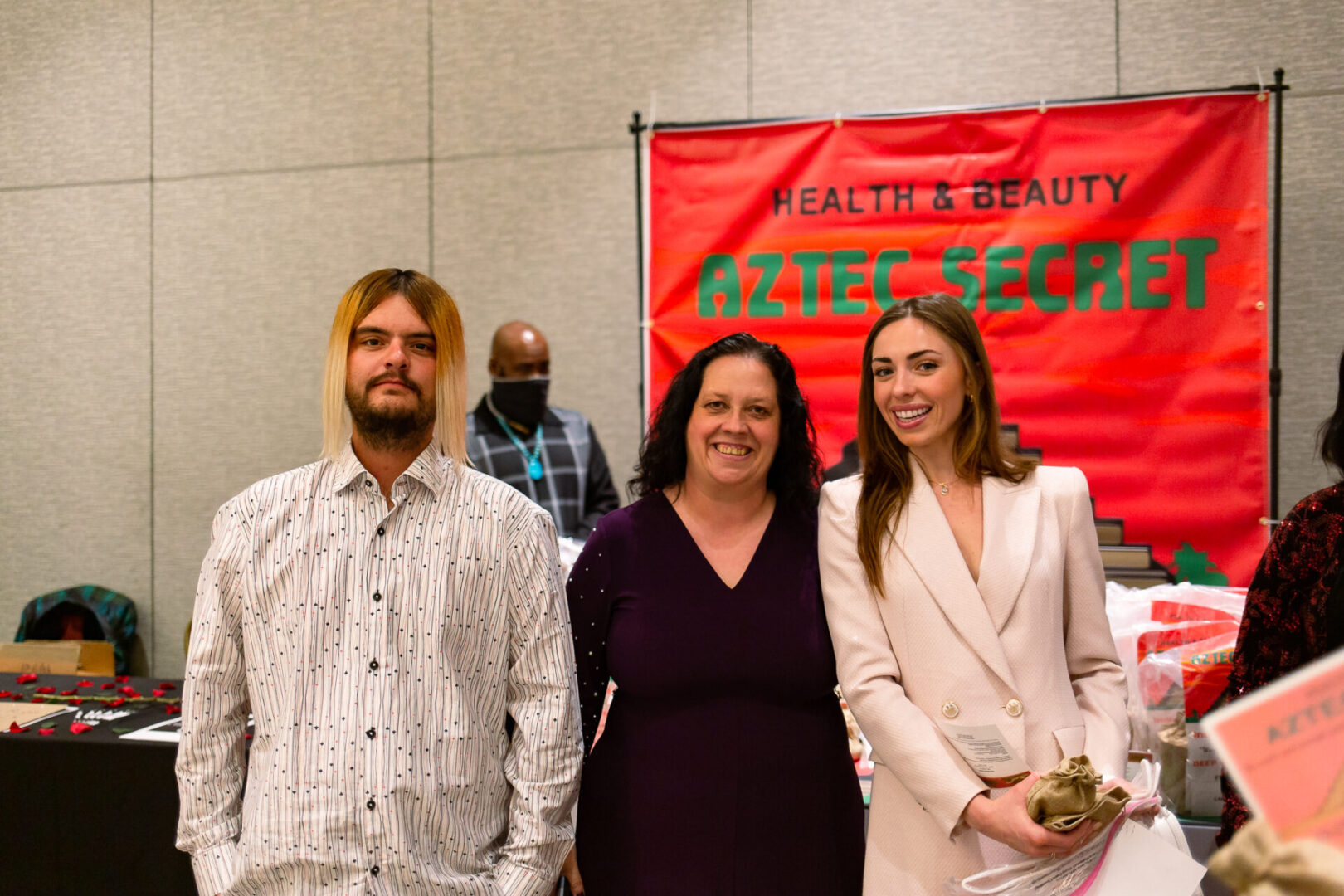 A man and two women posing in front of an Aztec Secret Health & Beauty LTD stall