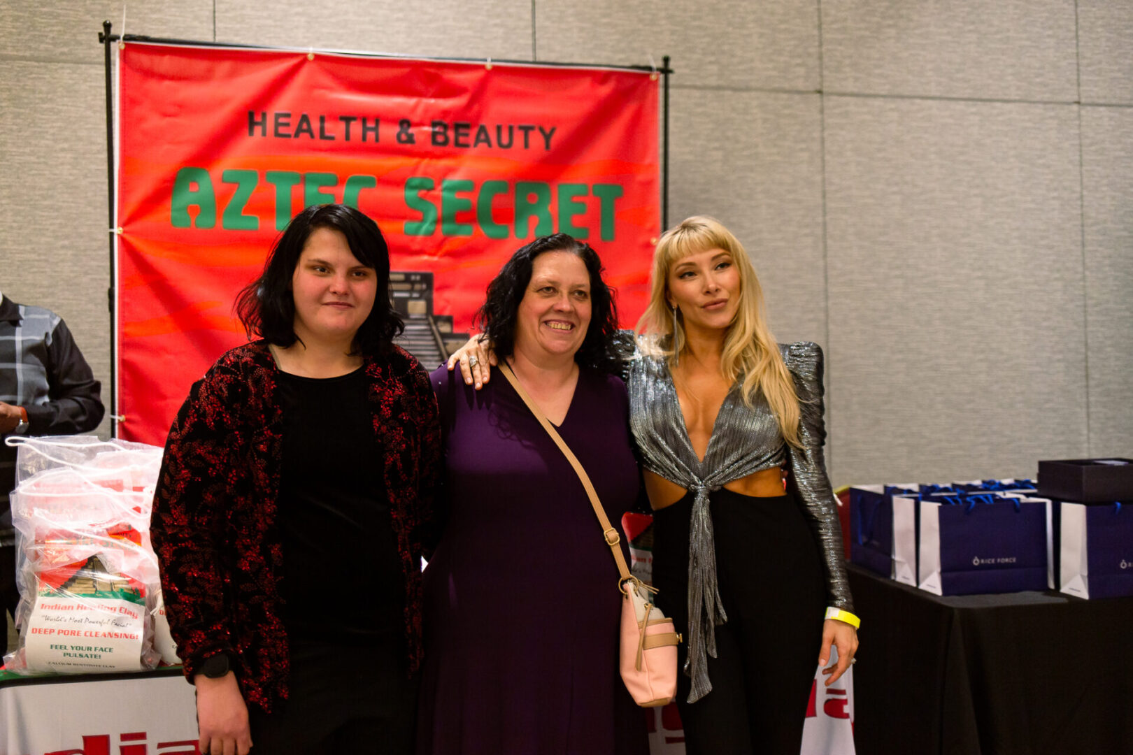 Three women posing in front of an Aztec Secret Health & Beauty LTD stall
