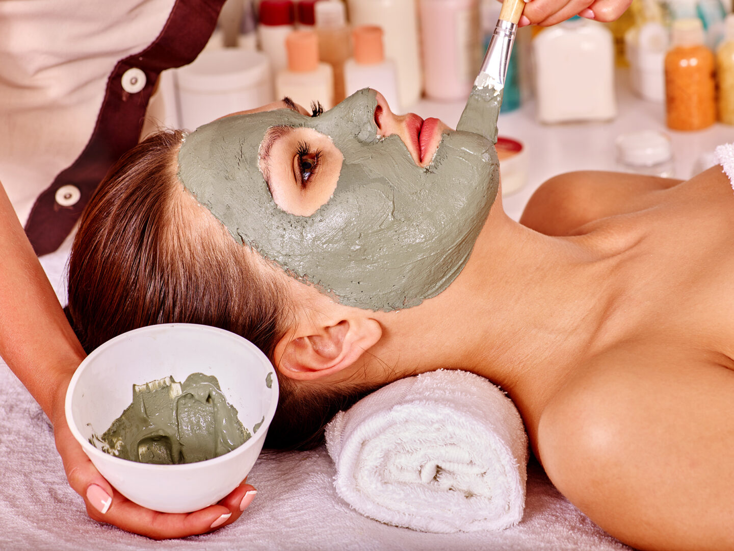 Woman with green clay facial mask in beauty spa.